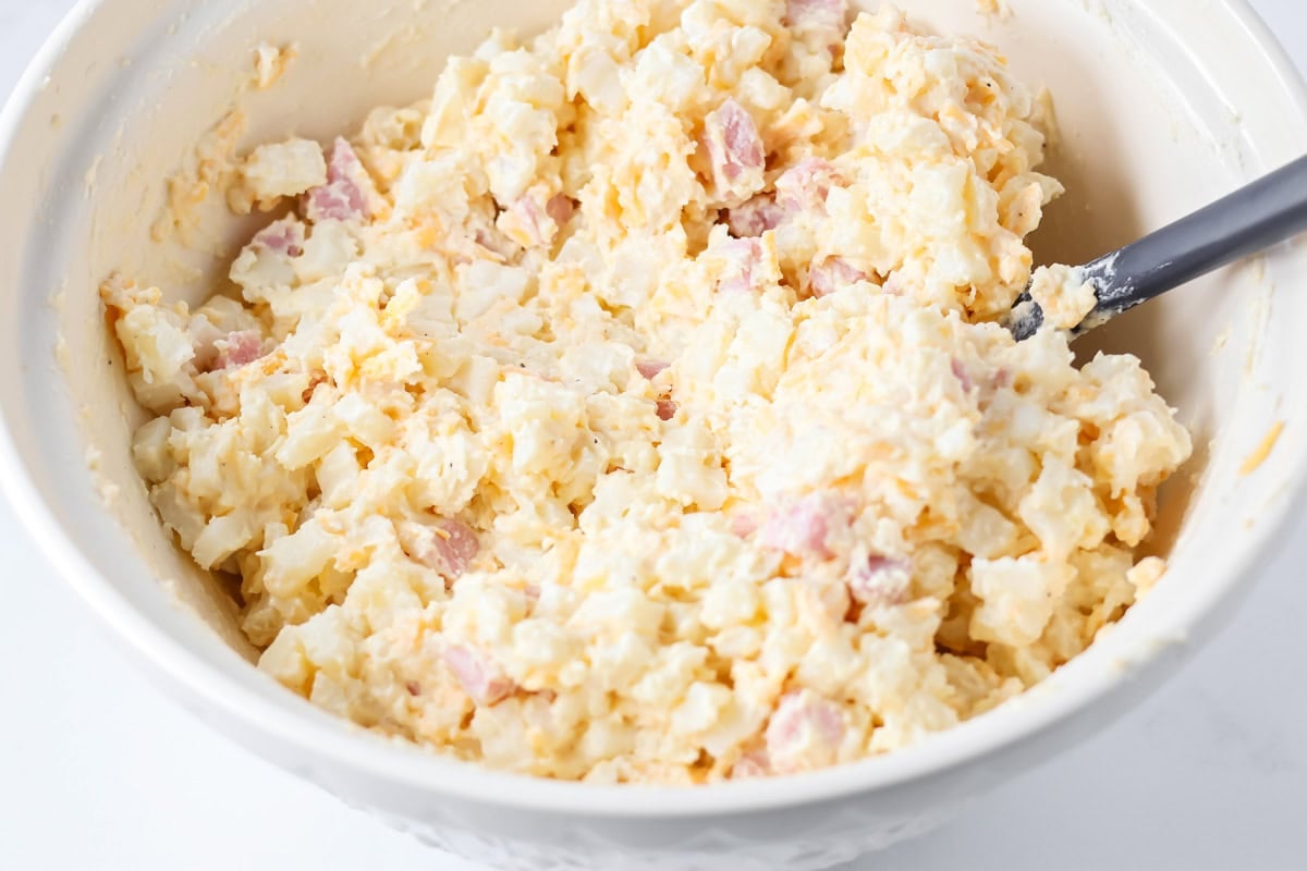 Ham and potato casserole ingredients mixed together in bowl.