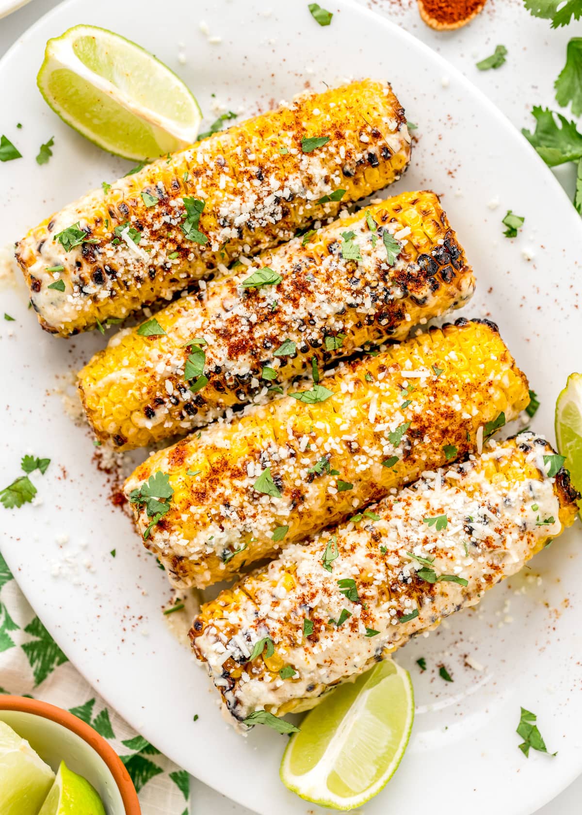 Seasoned Mexican corn on the cob on a white platter.