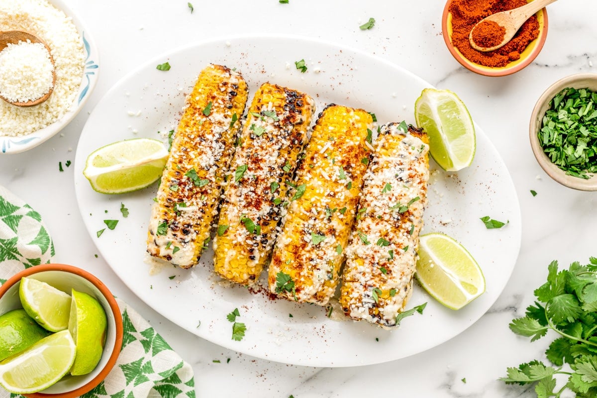 Vegetable side dishes - Mexican corn on the cob plated and topped with fresh herbs and cheese.