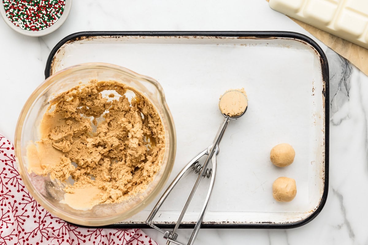 Scooping peanut butter snowballs from a bowl of dough.