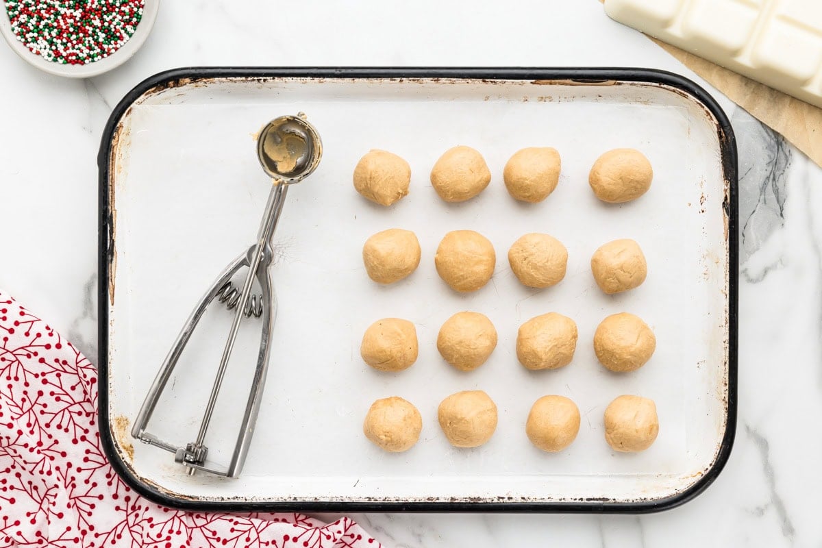 Scooping peanut butter snowballs and placing them on a lined baking sheet.
