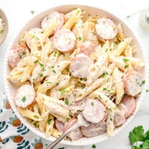 A bowl of sausage alfredo with fresh herbs as a garnish.