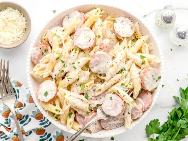 A bowl of sausage alfredo with fresh herbs as a garnish.