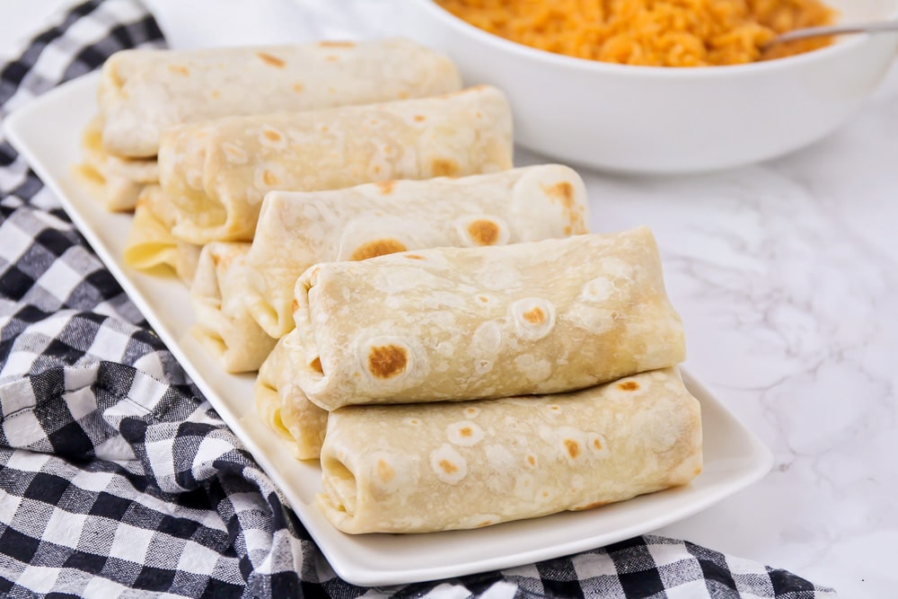 Bean burritos stacked on a white platter.