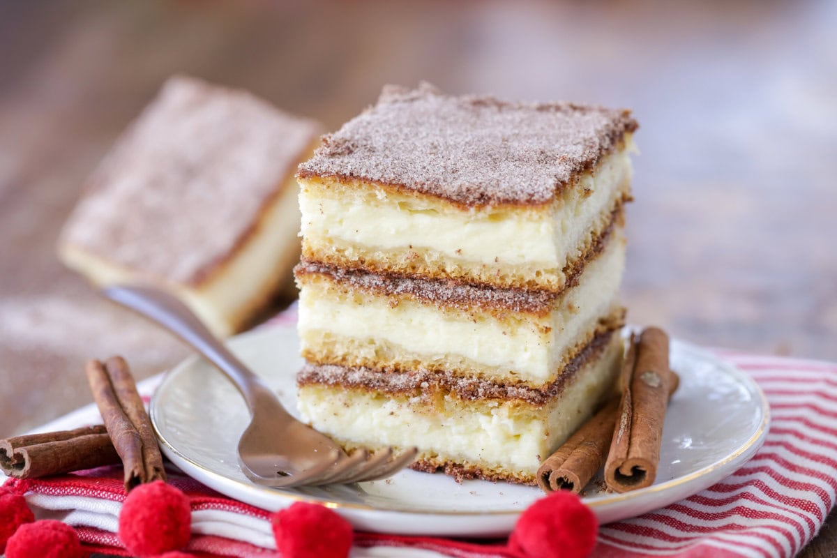 Three churro cheesecake bars stacked on a white plate.