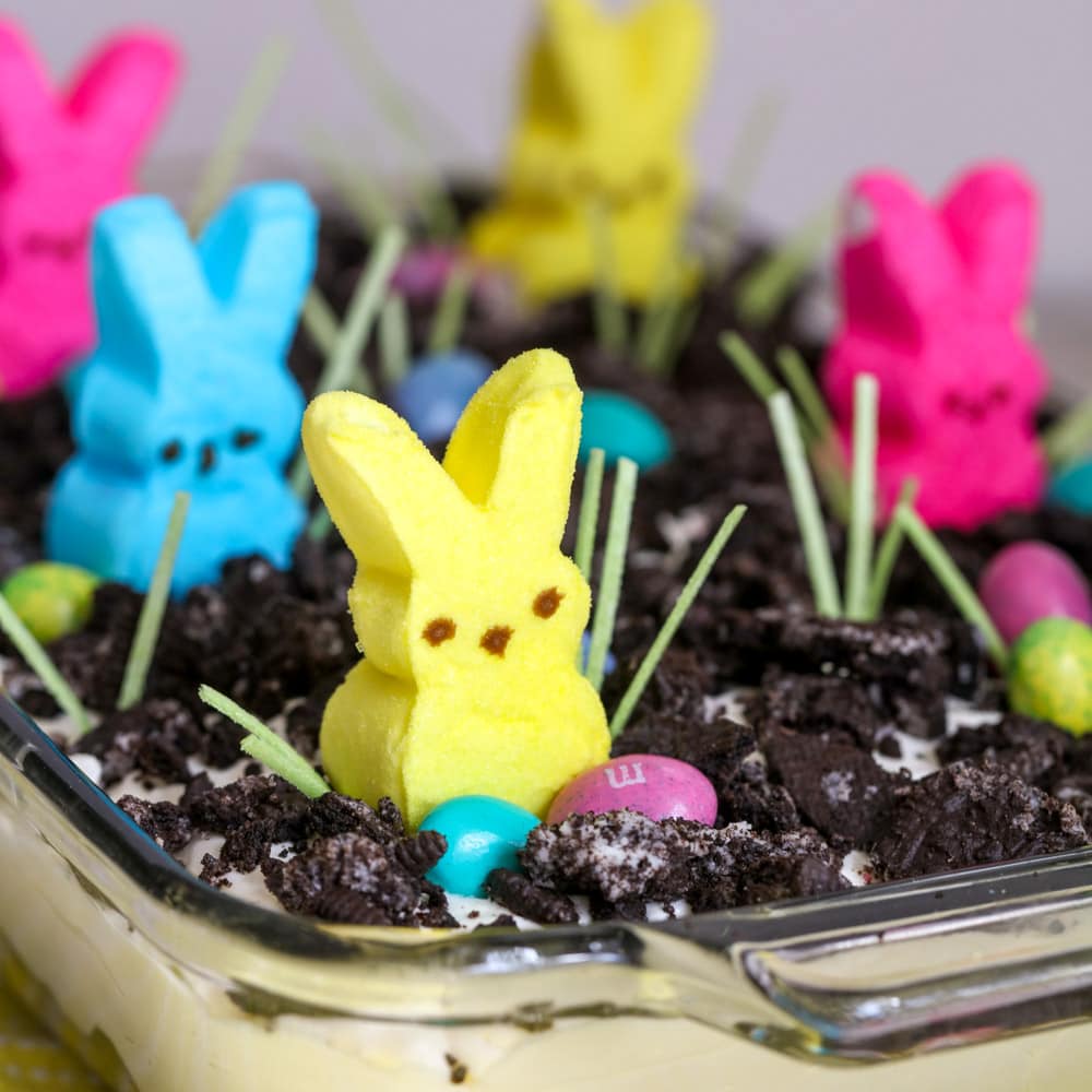 A clear casserole dish containing a pudding dessert topped with crushed Oreos, edible grass, Easter candies and Peeps.