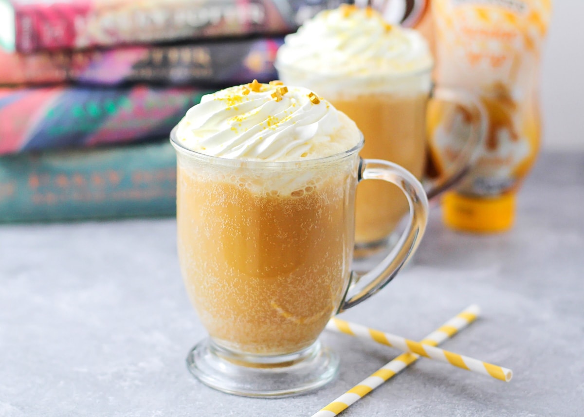 Glass mug filled with butterbeer and topped with whipped cream and sprinkles.