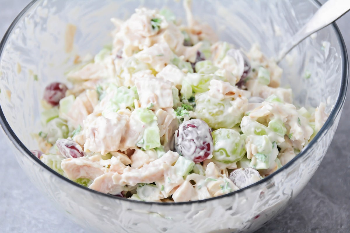 Mixing up chicken salad recipe  with grapes in a glass bowl.