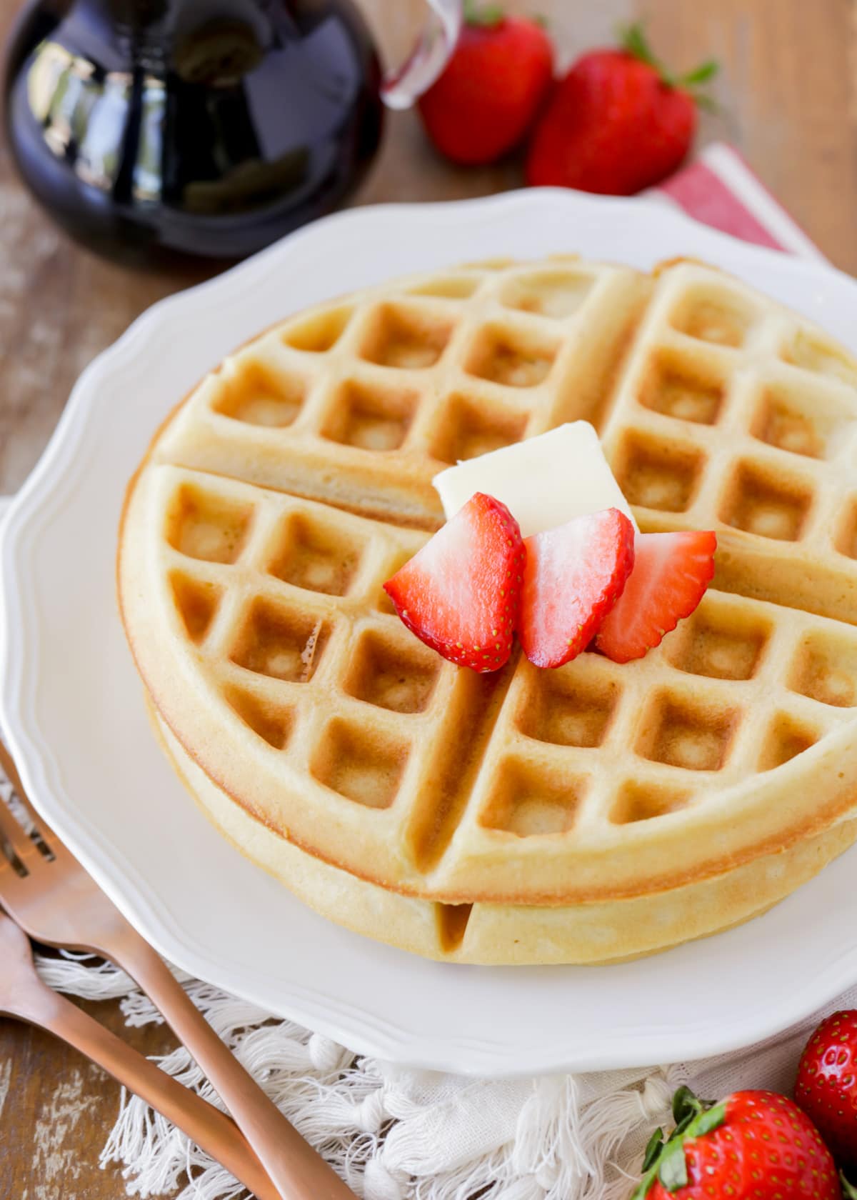 A white plate of crispy waffles topped with fresh strawberries.