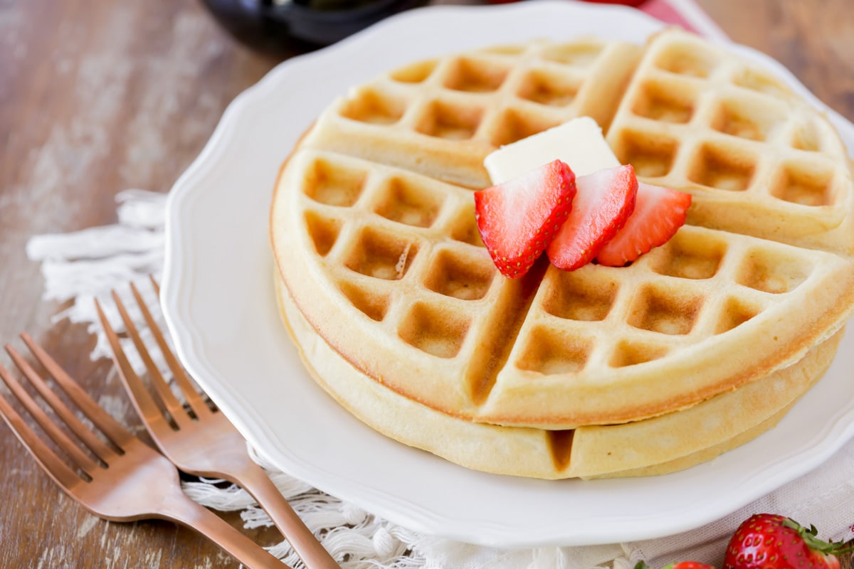 Two Crispy waffles on a white plate topped with fresh sliced strawberries and butter.