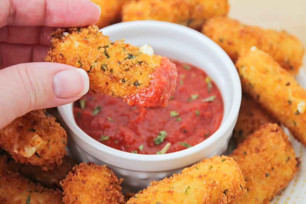 A homemade mozzarella stick being dipped in marinara.