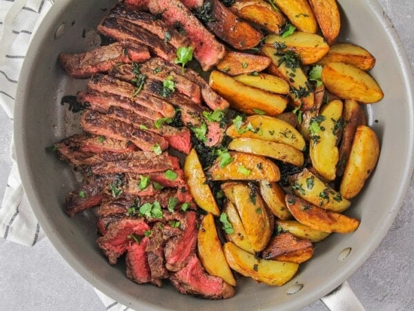 Sliced steak and potatoes in a skillet.