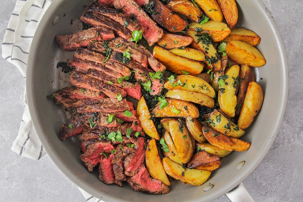 Sliced steak and crispy potato wedges in a pan for steak and potatoes.