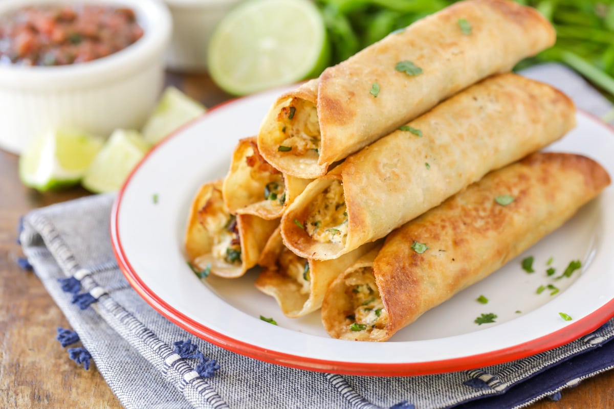 Chicken Taquitos stacked on white and red plate.