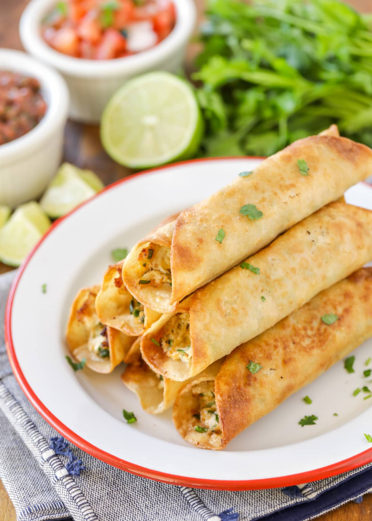 A close up of taquitos stacked on a white plate and sprinkled with fresh cilantro.