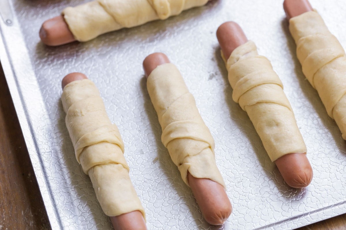 Hot dogs wrapped in crescent dough and placed on a baking sheet.