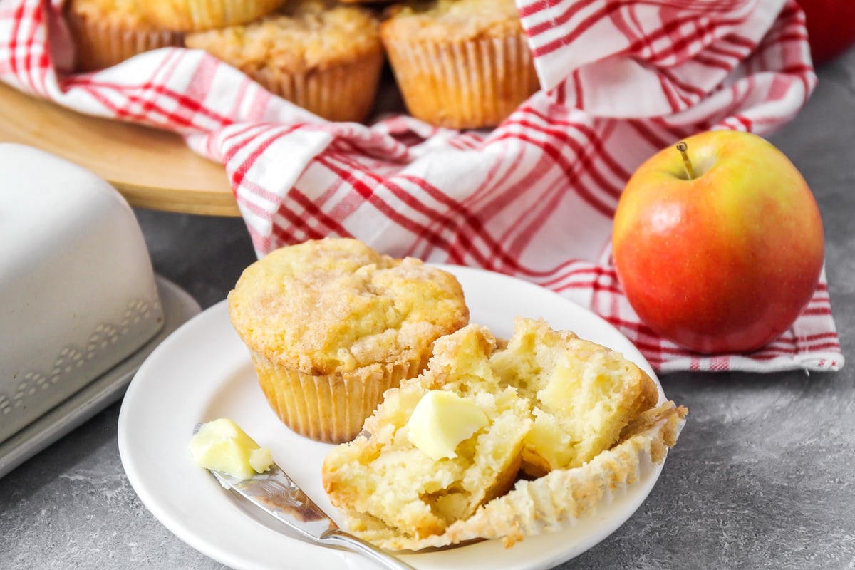 Apple muffins served on a white plate and topped with butter.