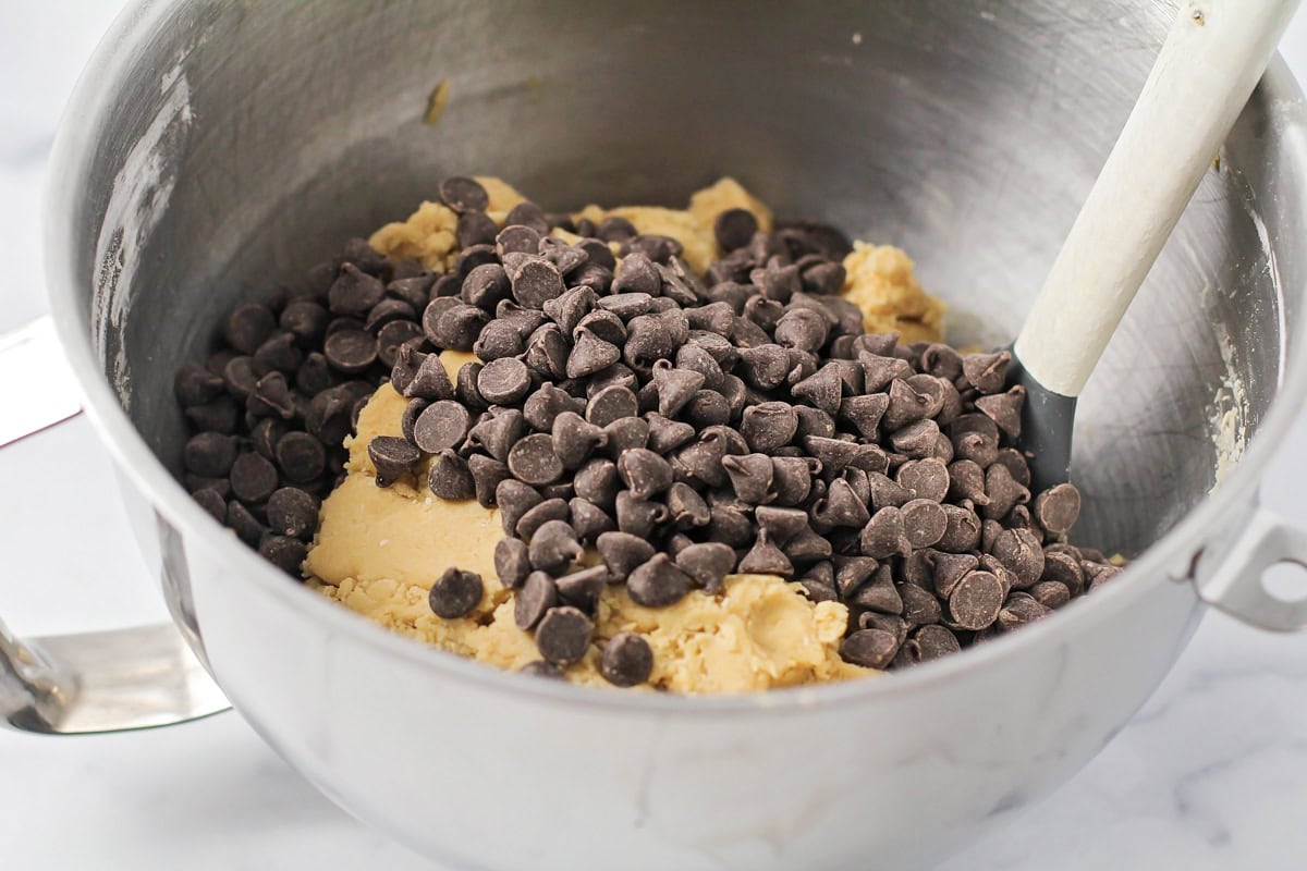 Chocolate chips poured over chocolate chip cookie dough in mixer.