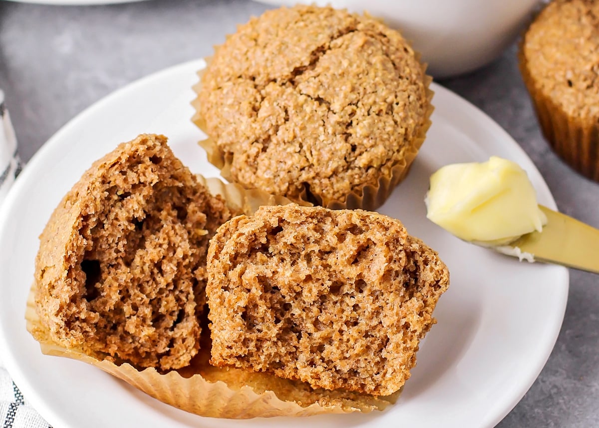2 bran muffins on a plate served with butter.