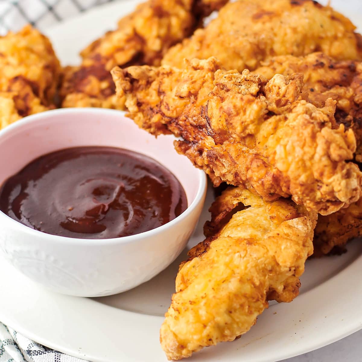 Close up of crispy chicken fingers recipe on a white plate with dipping sauce.