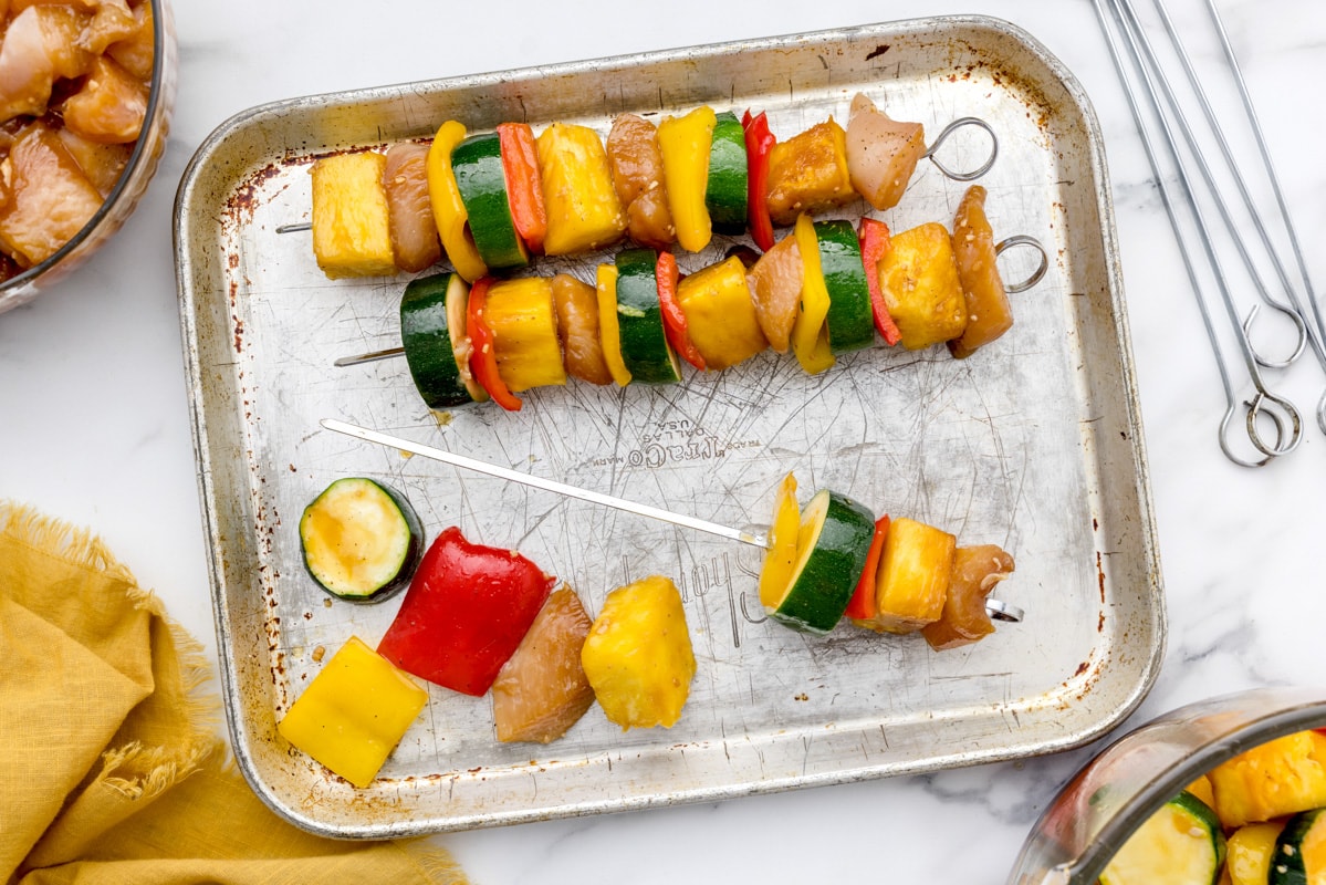 Assembling chicken kabobs on skewers for grilling.