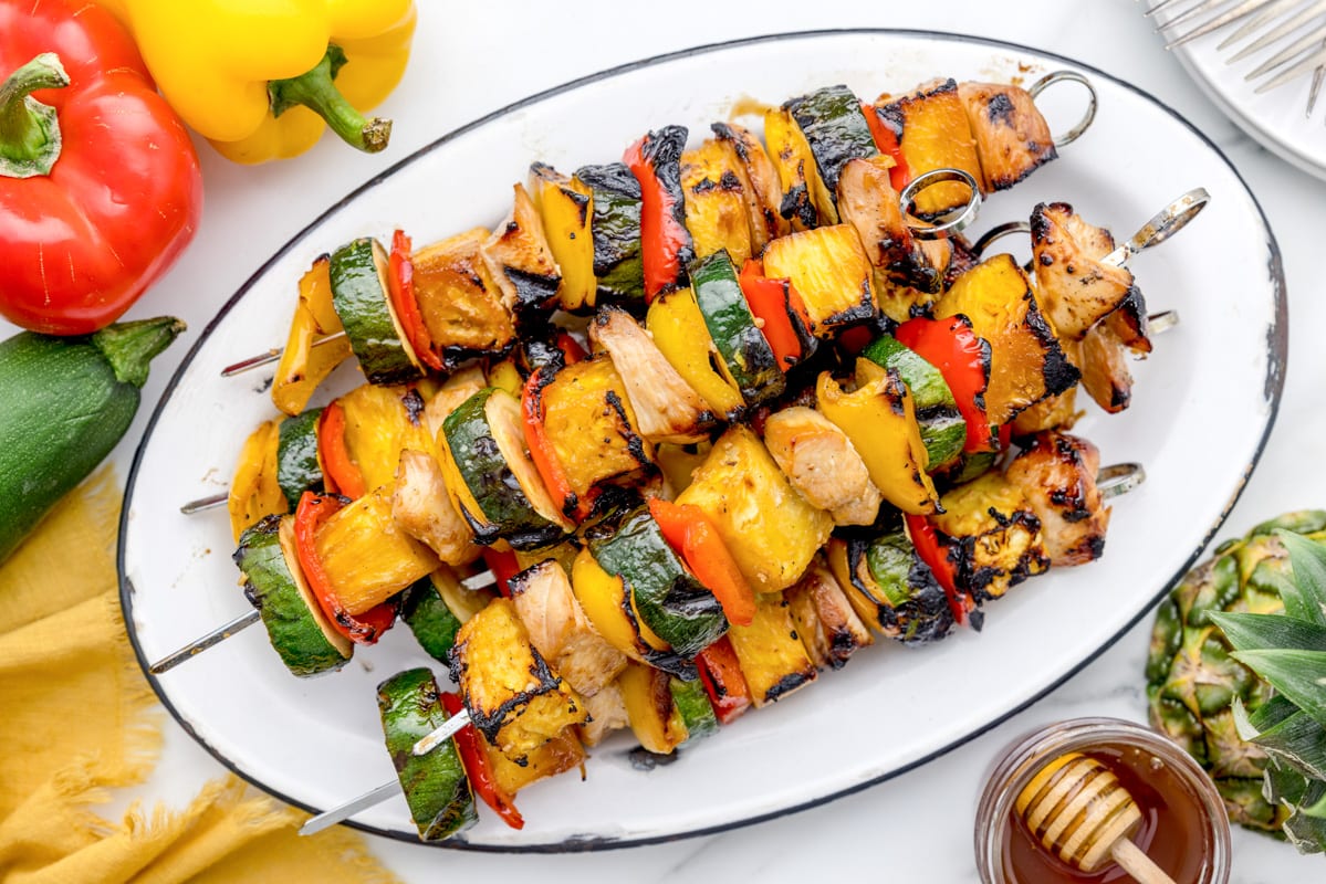 Grilled chicken kabobs on skewers on a white platter.