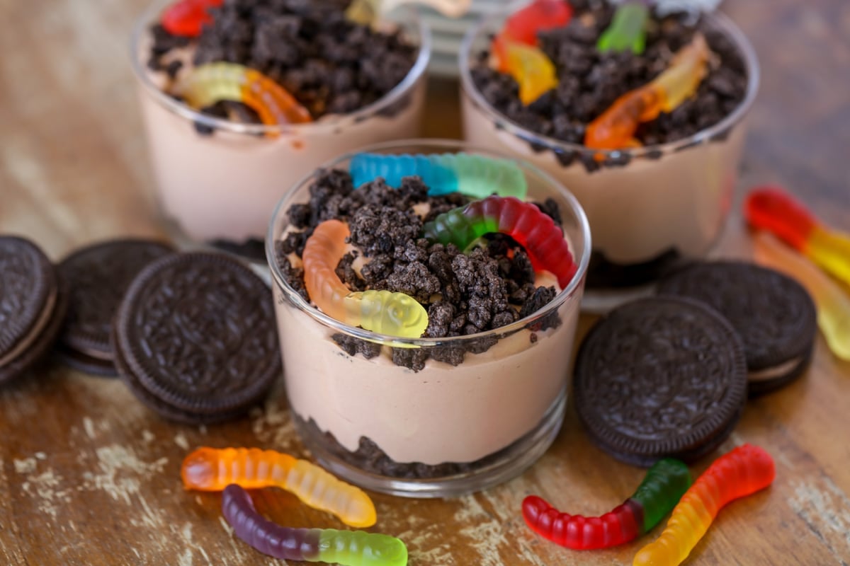 Dirt cake consisting of crushed oreo cookies, chocolate pudding and gummy worms in small glass cups. 