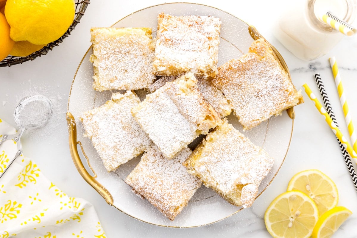 Lemon bars dusted with powdered sugar on a white gold rimmed plate. 