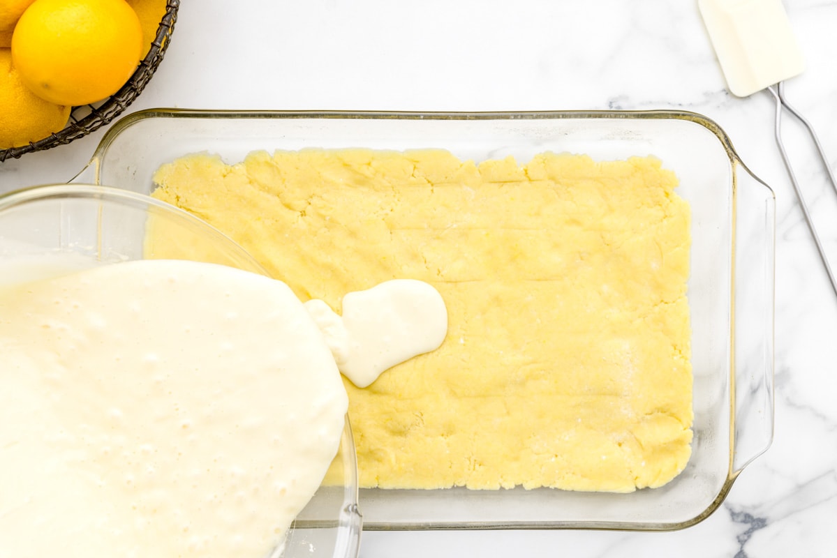 layering lemon bars with cake mix in a glass baking dish