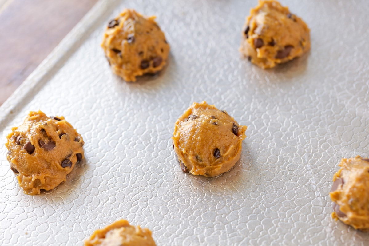Balls of mini pumpkin chocolate chip cookie dough on a baking sheet.