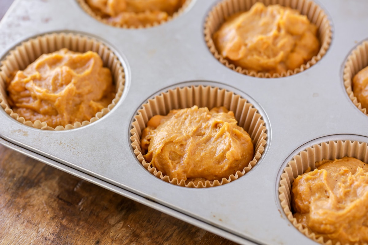 Schaufeln Sie den Teig in ausgekleidete Muffinformen für Kürbis-Butterscotch-Muffins.