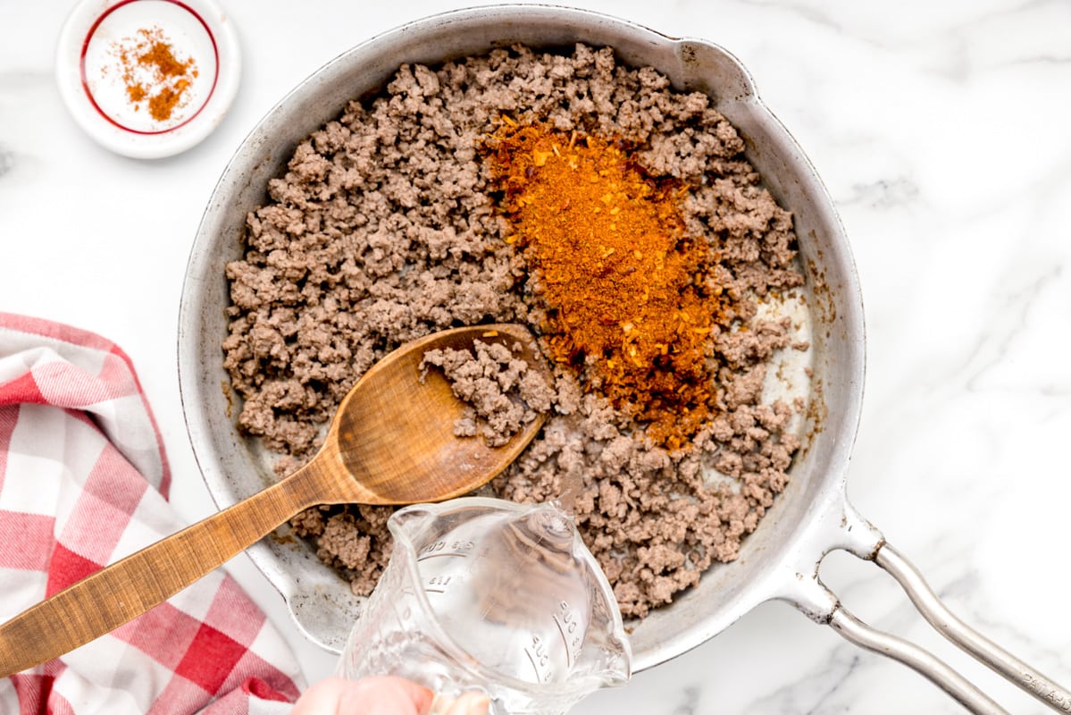 Seasoning and browning beef in a pan.