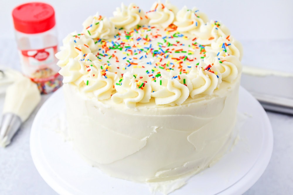 Vanilla cake from scratch on a cake stand being frosted.