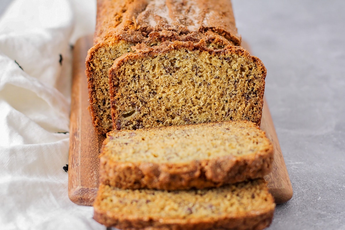 A loaf of banana bread with a few sliced pieces on a wooden cutting board. 