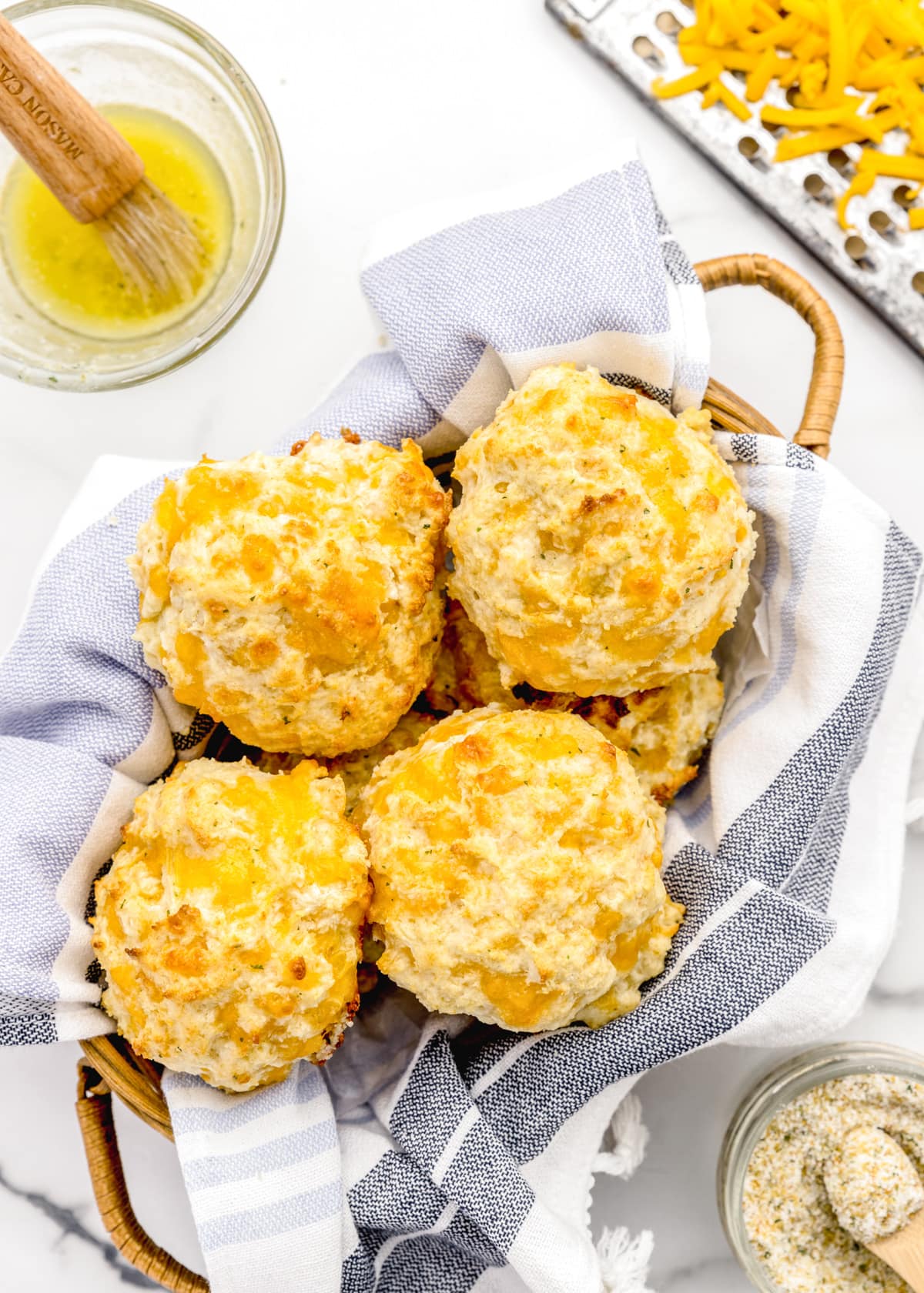 A basket filled with butter brushed cheddar biscuits.