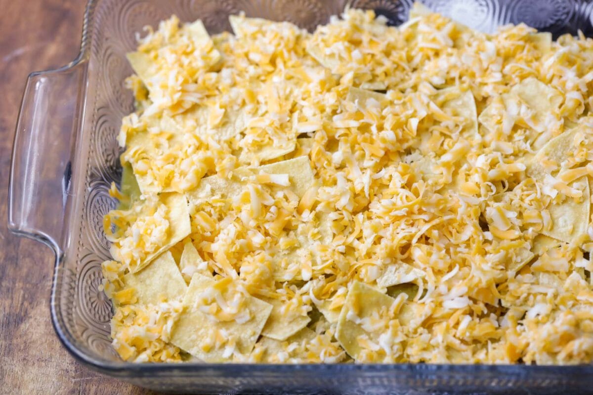 Chicken enchilada casserole process image - cheese, tortillas, sauce and more in baking dish.