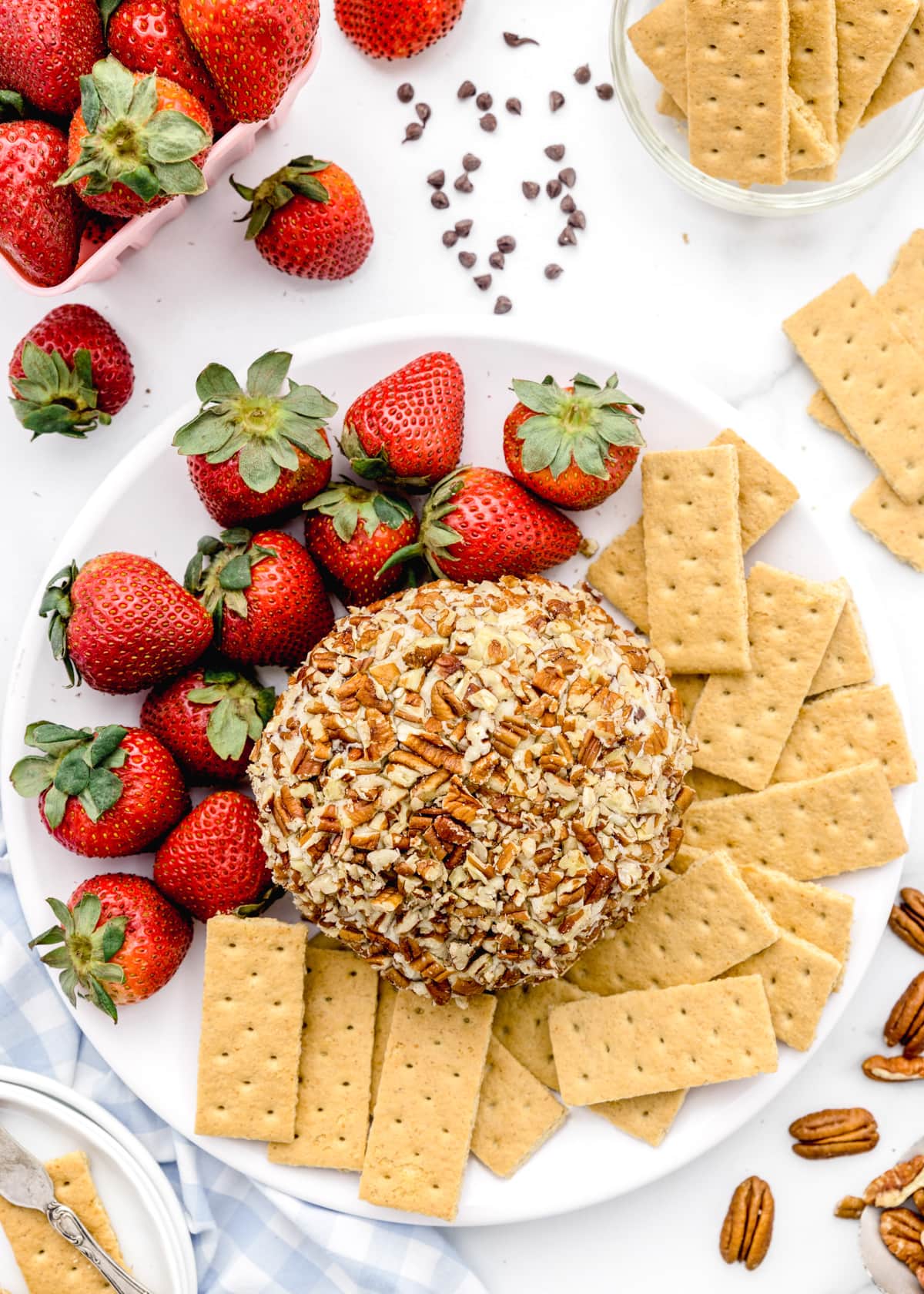 Plate of nut covered chocolate chip cheese ball served with strawberries and graham crackers.