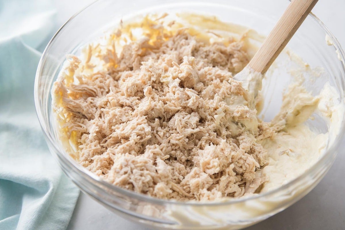 Shredded chicken being mixed with more ingredients in glass bowl.