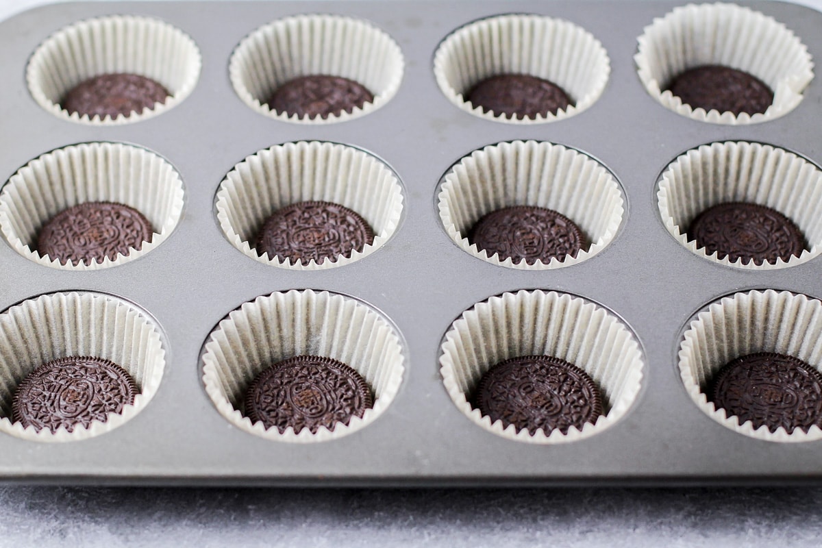 Muffin tin lined with oreo filled cupcakes liners for cookies and cream cupcakes.