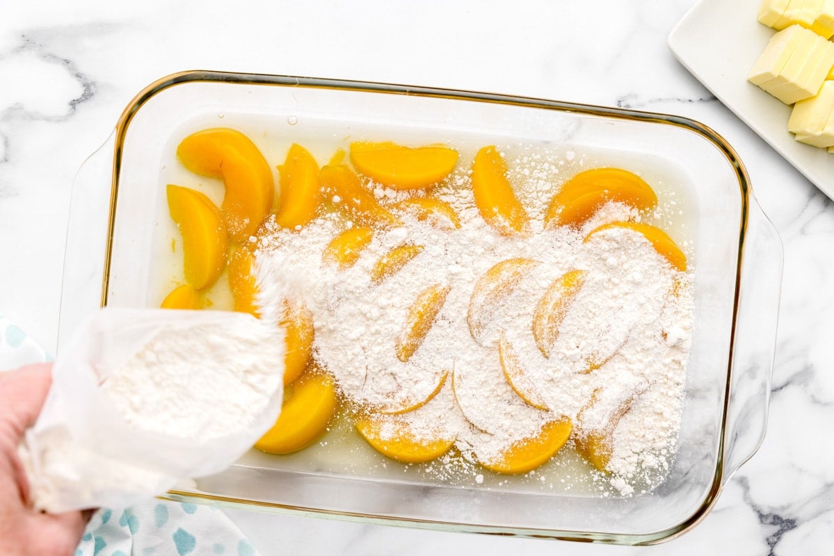 Peach cobbler with cake mix and canned peaches layered in a glass dish.