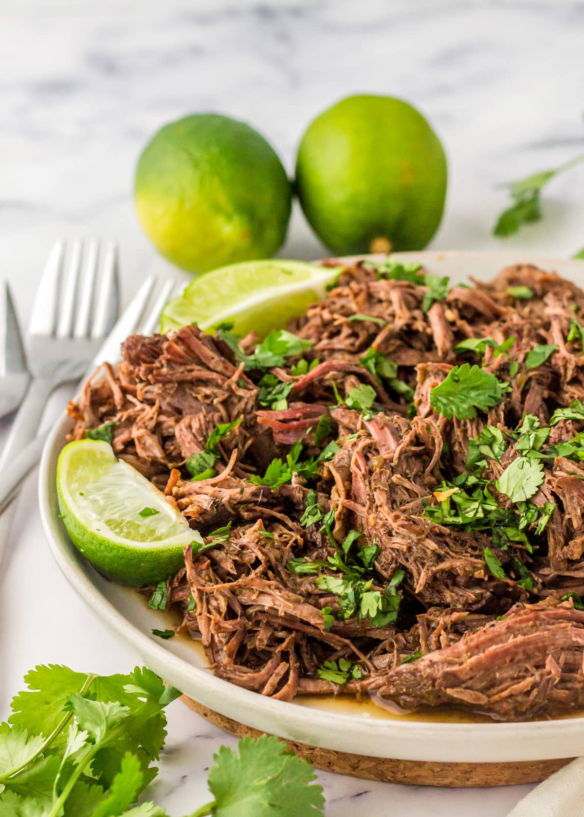 Shredded slow cooker barbacoa on a white plate served with lime slices.