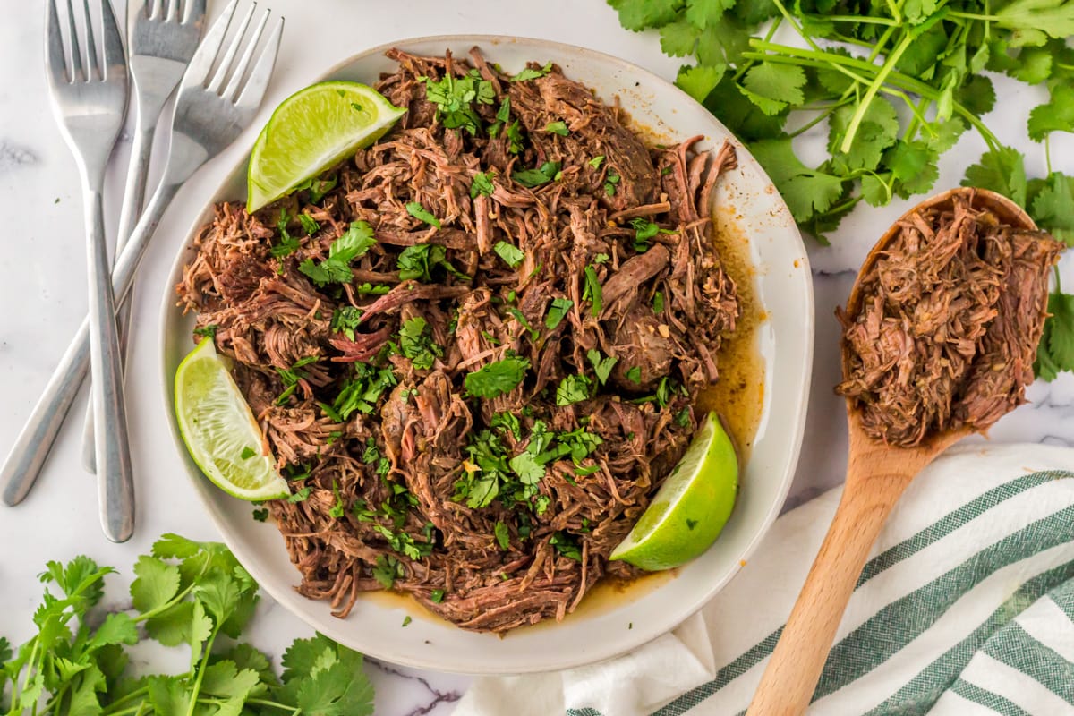 Slow cooker barbacoa on a plate shredded and served with lime wedges.