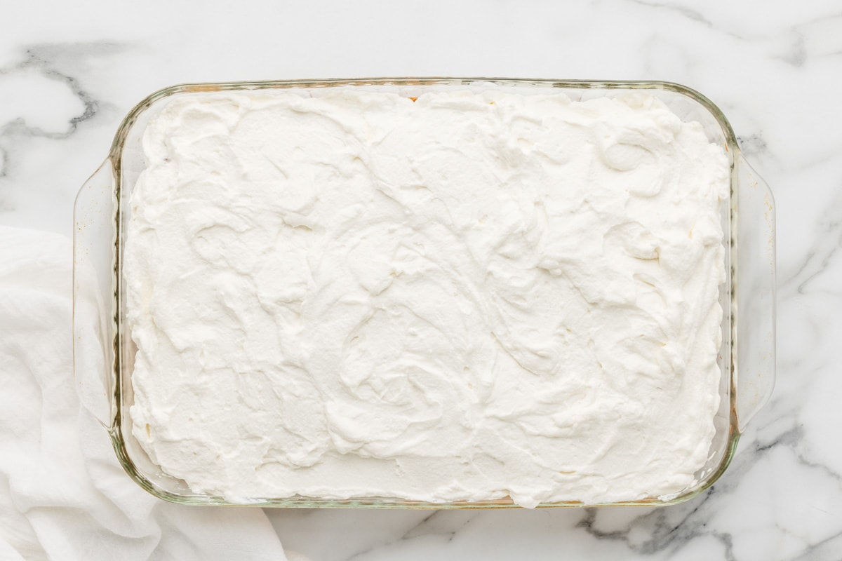 Topping the soaked tres leches cake recipe with whipped cream.