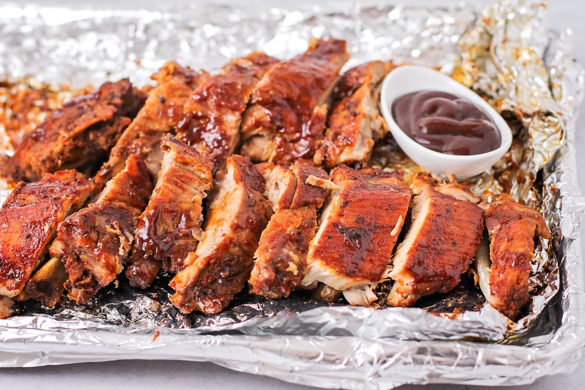 Sliced baby back ribs served with a side of bbq sauce.