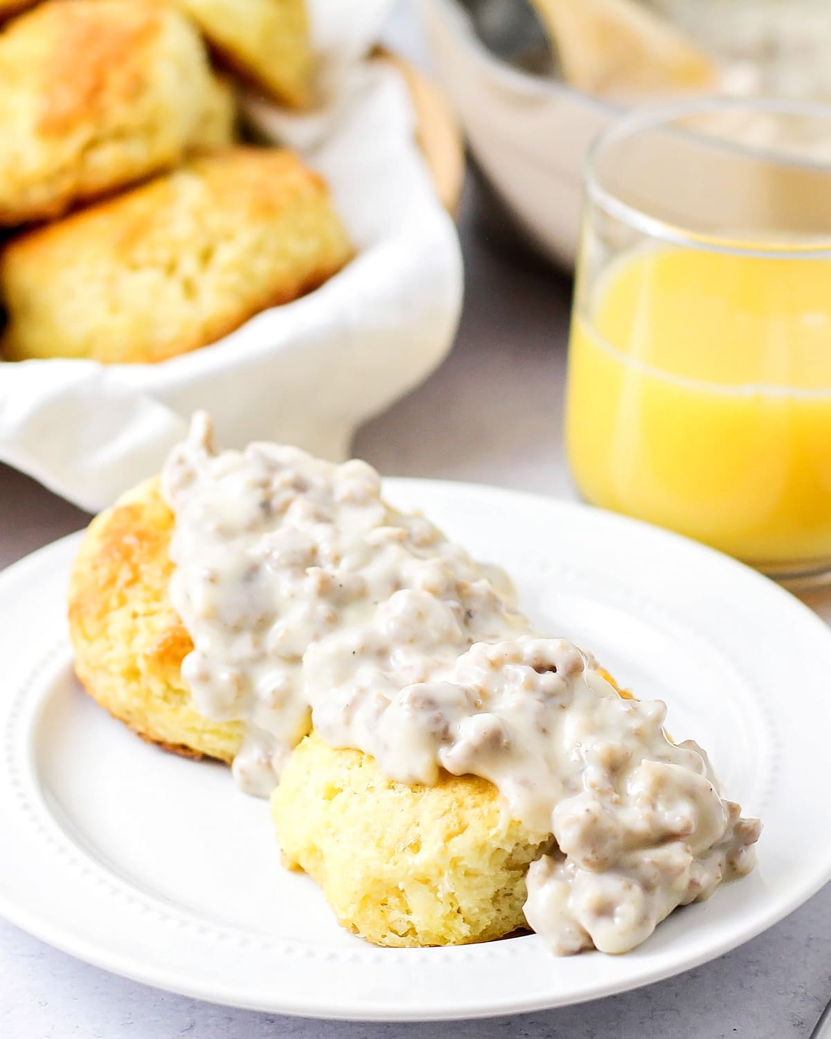 Biscuits and gravy on a white plate served with fresh orange juice.