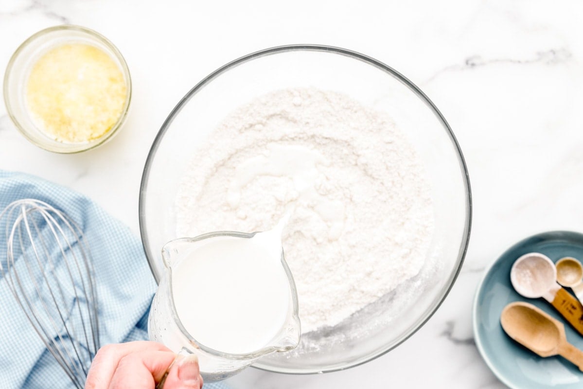 Adding milk to flour and other dry ingredients in a glass bowl.