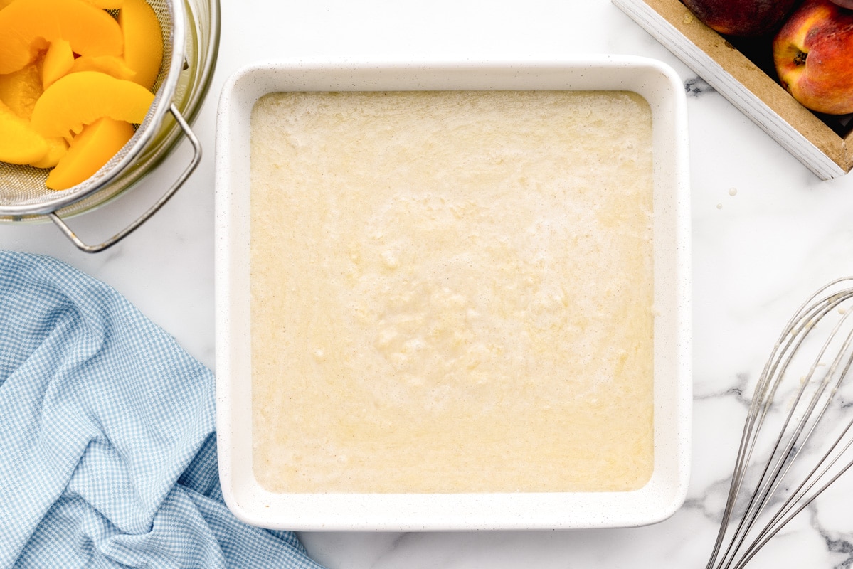 Homemade peach cobbler batter poured in baking dish.