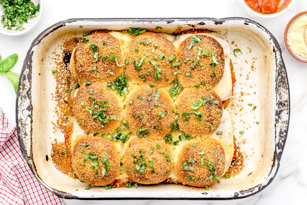 Herb topped chicken parmesan sliders in a baking dish.
