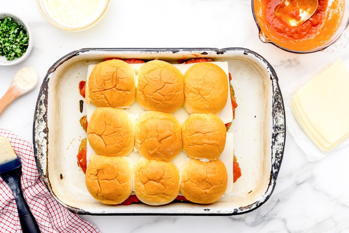 Placing buns on top of chicken parmesan sliders.