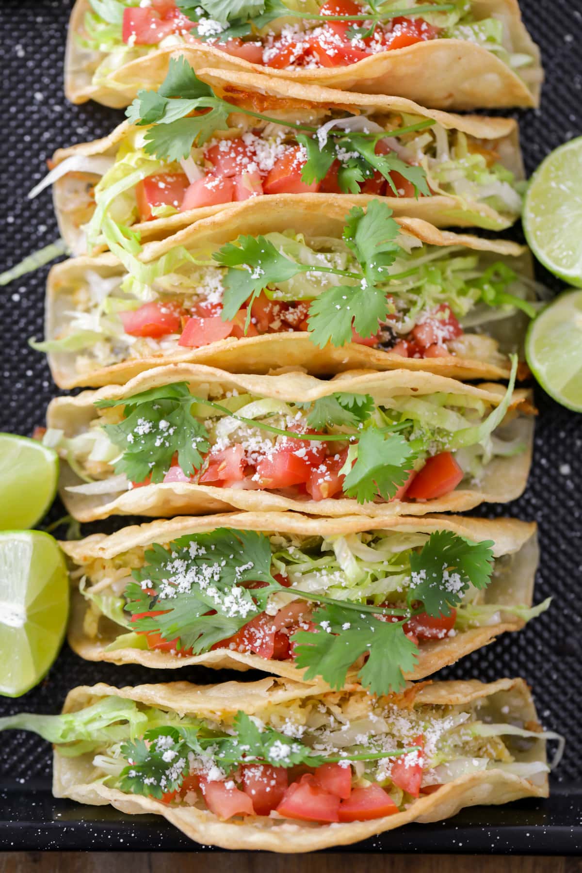 Six Chicken tacos lined up on a gray plate.
